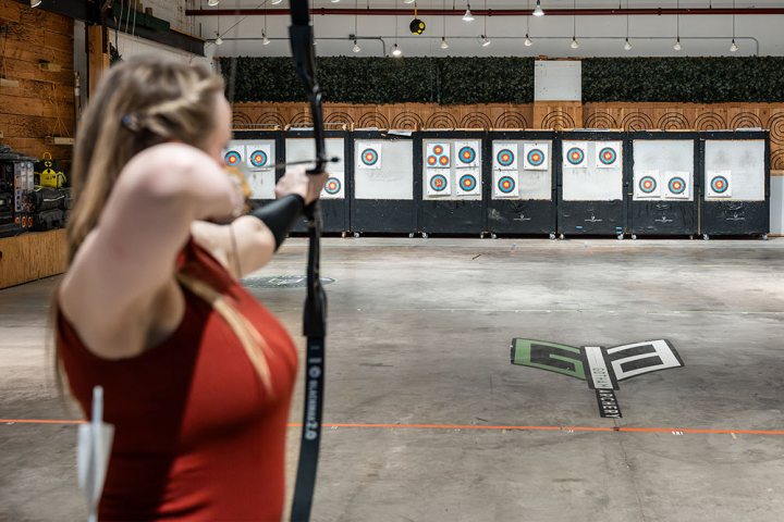 Person practicing archery aiming at targets in an indoor range.