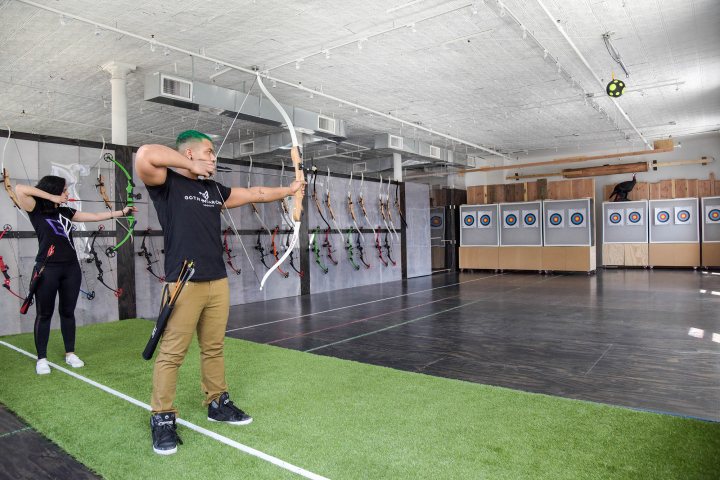 Two people practicing archery indoors, aiming at targets.