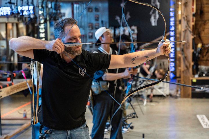 Man practicing archery indoors with a bow and arrow.