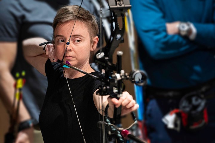 Person aiming a bow and arrow in an archery event.