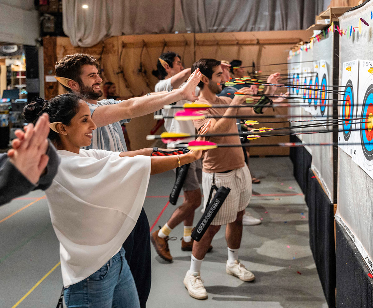 People practicing archery indoors aiming at targets.