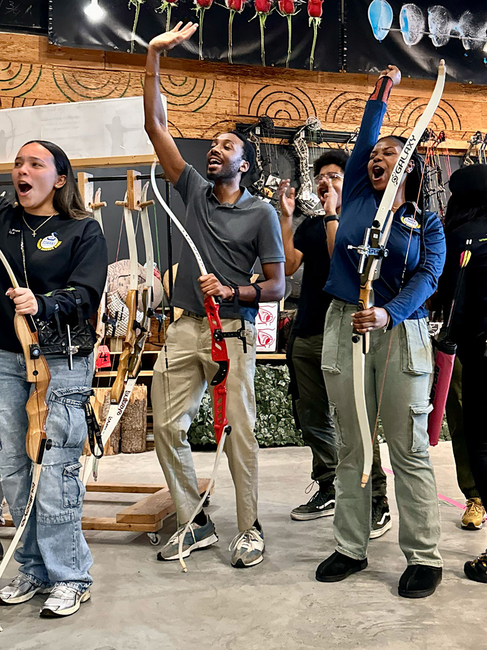Group holding bows, cheering inside an archery shop.